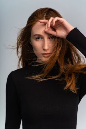 Beautiful ginger woman in dark sweater looking at camera and posing on grey studio backgroundの写真素材