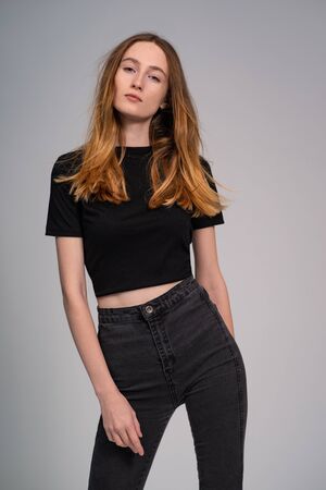 Beautiful ginger woman in dark clothes looking at camera and posing on grey studio backgroundの写真素材