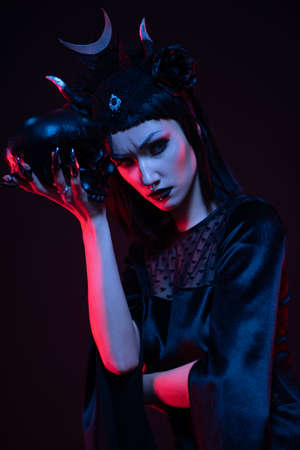 Brunette model in gothic black outfit posing with skull in studioの写真素材