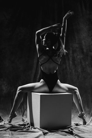 Girl gymnast posing on white cubes in black swimsuit in studio. Black and white portraitの写真素材
