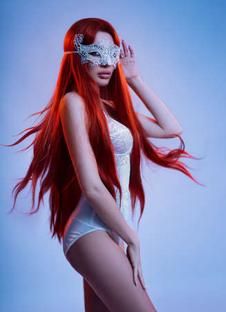 Young woman in carnaval mask and white lingerie posing in studioの写真素材