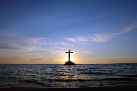 Colorful sunset over Sunken Cemetery on the tropical island of Camiguin. The cross in the sea is a memorial for the victims of the 1871 volcanic eruption here, when the ancient capital Cotta Bato was destroyed by the lava.の写真素材