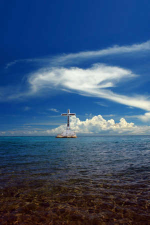 Sunken Cemetery on the exotic island of Camiguin. Seascape and sky with majestic tropical clouds. The cross is a memorial for the victims of the 1871 volcanic eruption here, when the ancient capital Cotta Bato was destroyed by the lava.の写真素材