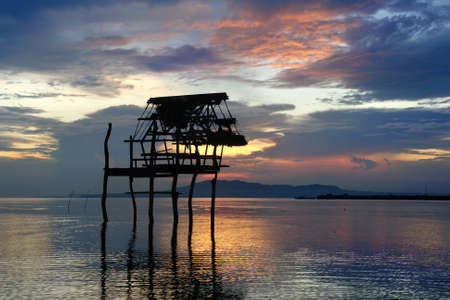 Flamboyant, exotic, tropical and colorful sunset over sea and mountains with a pole house skeleton silhouette in front in the water. Bohol, Philippines.の写真素材