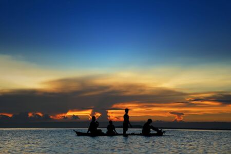 Asian children's silhouette in a canoe at sea in front of a tropical flamboyant sunset.の写真素材