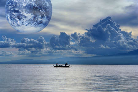 Blue gloomy sunset on a tropical sea with a cloudscape and globe, and fishermen in a small boat leaving for the nightly catch. Metaphor of water, source of global life on the planet. Globe is public domain photo of NASA.の写真素材
