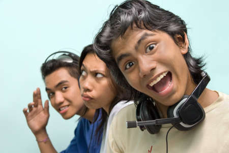 Portrait of three young Asian callcenter, telephone helpdesk or support center agents, faces lined up in a row and with headset, relaxing during break or work time making funny grimaces.の写真素材