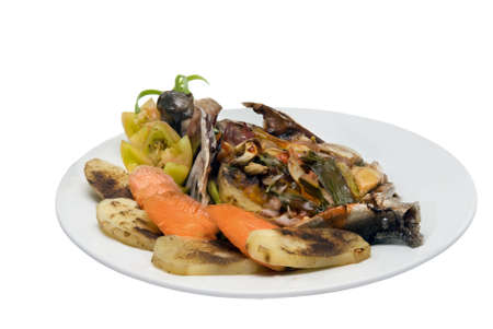 Tropical and exotic healthy low-calories cooked fish and veggies food dish with tomatoes, potatoes, carrots, spices and greens. Isolated over white.の写真素材