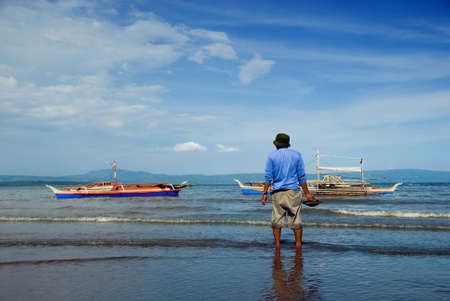 Asian fisherman waiting in the waves for the returning fishermen's boats with the day catch.の写真素材