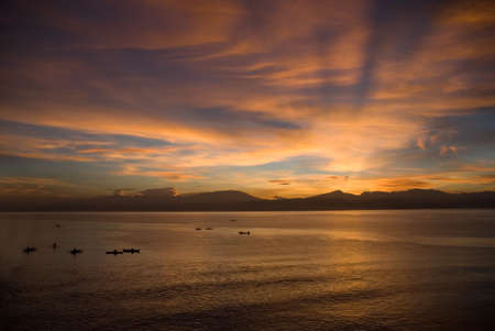 Flamboyant colourful early exotic sunrise or dawn over a tropical bay with majestic orange sky and fishermen's boats on the sea surface.の写真素材
