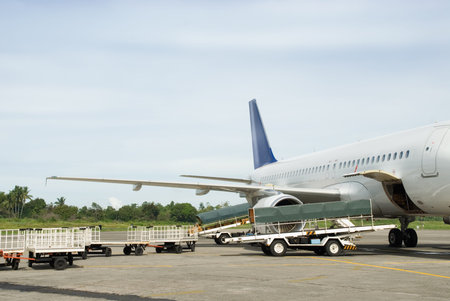 Commercial airliner or airplane with open cargo bays parked on the tarmac of a tropical airport with...