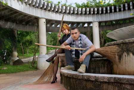 Teenage punk or emo Asian couple posing with broom in a deserted urban environment. Concept of diversity and teen emo lifestyle.の写真素材