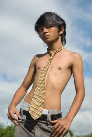 Teenage Asian skinny shirtless boy with necktie and in jeans striking a fashion pose outdoors.の写真素材