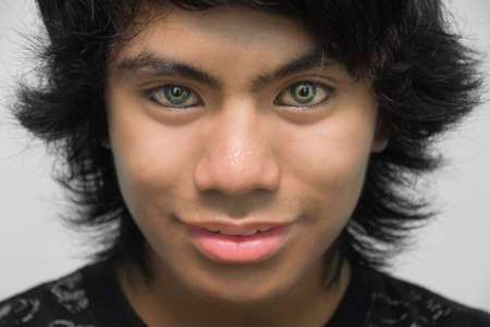 Closeup cropped portrait of smiling punk or emo Indian teenager with eyeliner and green contact lenses: emphasis on the eyes.の写真素材