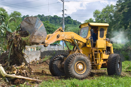 A worn, recycled bulldozer with polluting smoke plume clearing plant debris and soilの写真素材