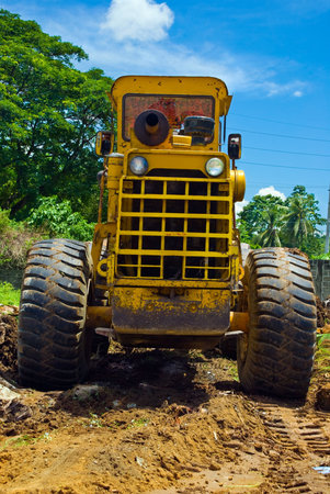 Back view of a worn and rusted bulldozer or earthmover leveling residential tropical terrain with...