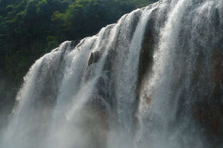 Detail closeup of a wide tropical waterfall edge with droplets, haze and water mist, and whitewater on a jungle background.の写真素材