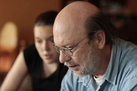 Close up portrait of bald senior man looking down pensive or worried with blurred grandchild girl face in the background.の写真素材