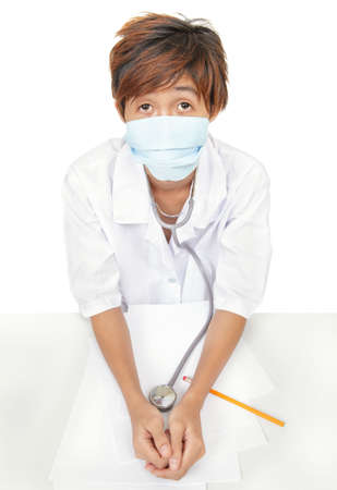 Young Korean doctor sitting on desk looking worried, with surgical mask afraid to get infected. Isolated over white.の写真素材