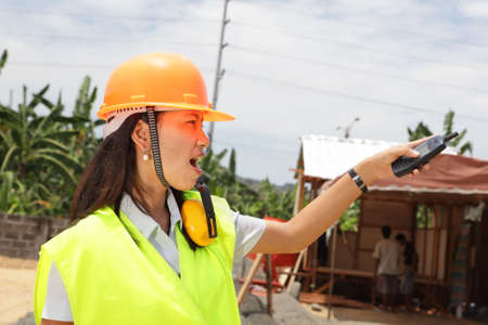 Pointing young Chinese female engineer with hardhat, directing and supervising a residential tropical construction site.の写真素材