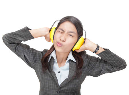 Ironic Asian businesswoman, winking and pouting lips, shutting out communication ostensibly by firmly pressing ear-protectors against her ears. Isolated over white with copyspace.の写真素材