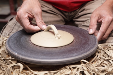 Close-up view of  potter's hands attaching ear or handle to the lid or cover of a clay vase or bowl in a pottery.の写真素材