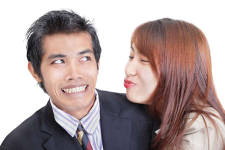 Young Asian businesswoman or office worker trying to approach and to kiss her male colleague that  apparent by his reluctant and embarrassed facial expression, seems to dislike her overture. Duo portrait isolated over white. Concept of sexual harassment aの写真素材