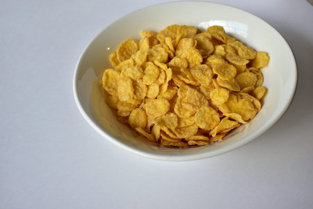 A Cup of yellow cornflakes in milk on a white background.