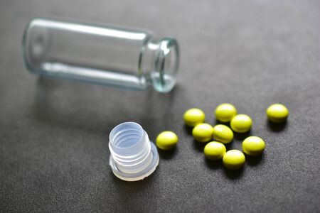 Glass jar and yellow tablets on a black backgroundの写真素材