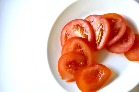 Ripe and juicy tomatoes sliced on a white plateの写真素材