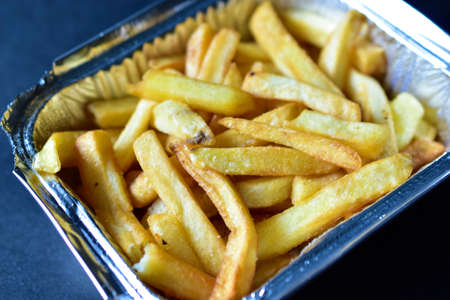 Delicious French fries in an aluminum container on a black backgroundの写真素材