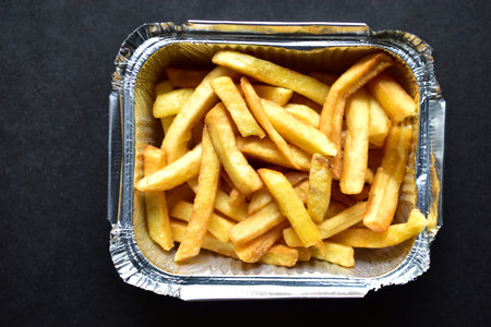 Delicious French fries in an aluminum container on a black background
