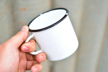 White metal enameled mug in the hands of a personの写真素材