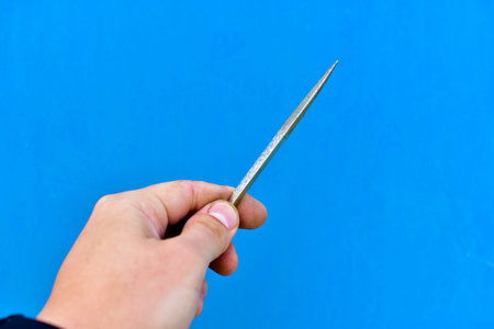 Small tool file in hand on a blue backgroundの写真素材