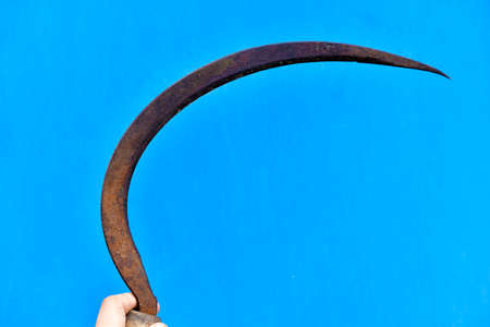 Iron sickle in hand on a blue backgroundの写真素材