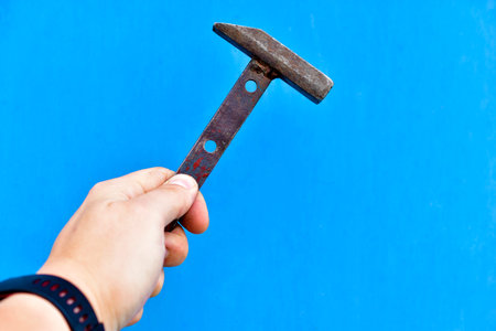 Small metal hammer in hand on a blue background