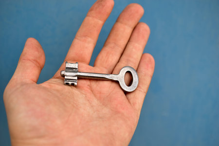 Old iron door key in hand on blue background