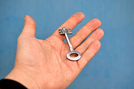 Old iron door key in hand on blue backgroundの写真素材