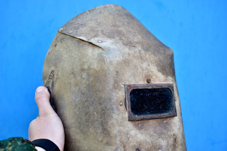 Protective welding shield in hand on a blue background