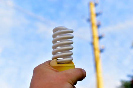 Twisted fluorescent lamp in hand against the background of a power lineの写真素材