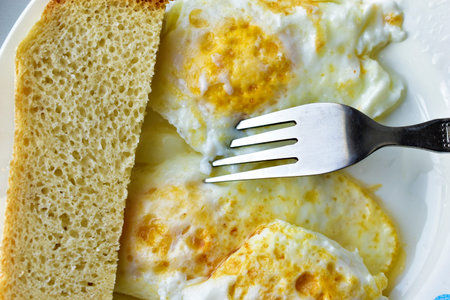 Three fried eggs on a plate with bread and a fork