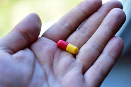 Yellow red pill in hand during the dayの写真素材