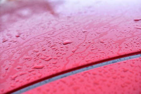 The surface and glass of the red car covered with raindropsの写真素材
