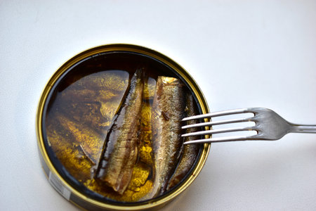 Sprats in oil in a jar with a fork on a white backgroundの写真素材