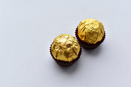 Round chocolate candies in a gold wrapper on a white background