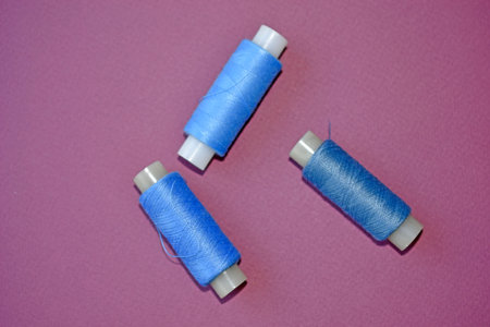 Blue spools of thread on a purple background with needles