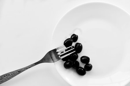 Pickled black olives on a white plate with a forkの写真素材