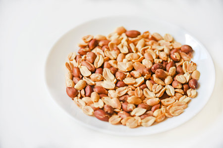 Fried delicious peanuts on a white plate close-up. Healthy food, diet.