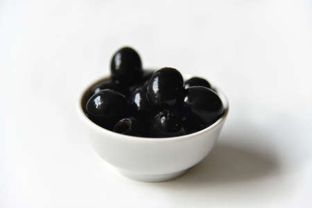 Black olives in a white and glass saucepan on a white background. Vegetarian food.の写真素材