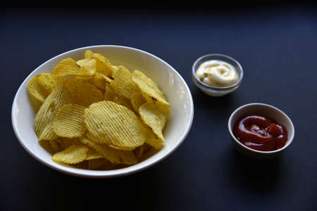 Delicious potato chips with sauces on a black background. Appetizer of potato chips with sauce. Fast food on a black background.の写真素材